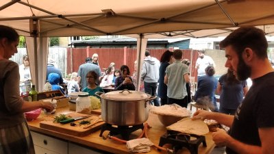 lots of people are milling around an outdoor kitchen where food is being prepared.