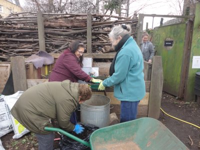 3 elders sieve compost by some compost bays, smiling.